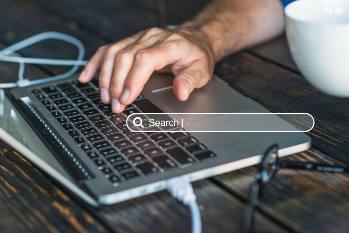 Une main tapant sur un clavier d'ordinateur portable avec une barre de recherche en surimpression