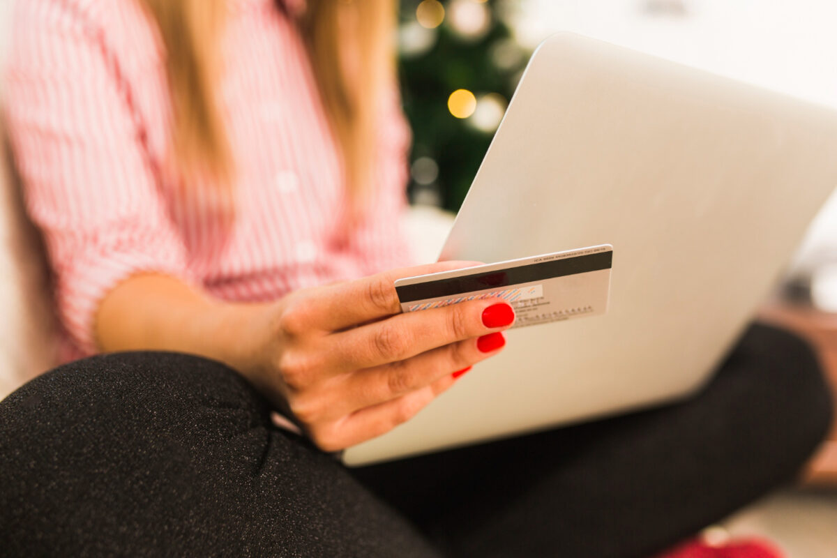 Femme tenant une carte bancaire devant un ordinateur portable, faisant des achats en ligne près d'un sapin de Noël