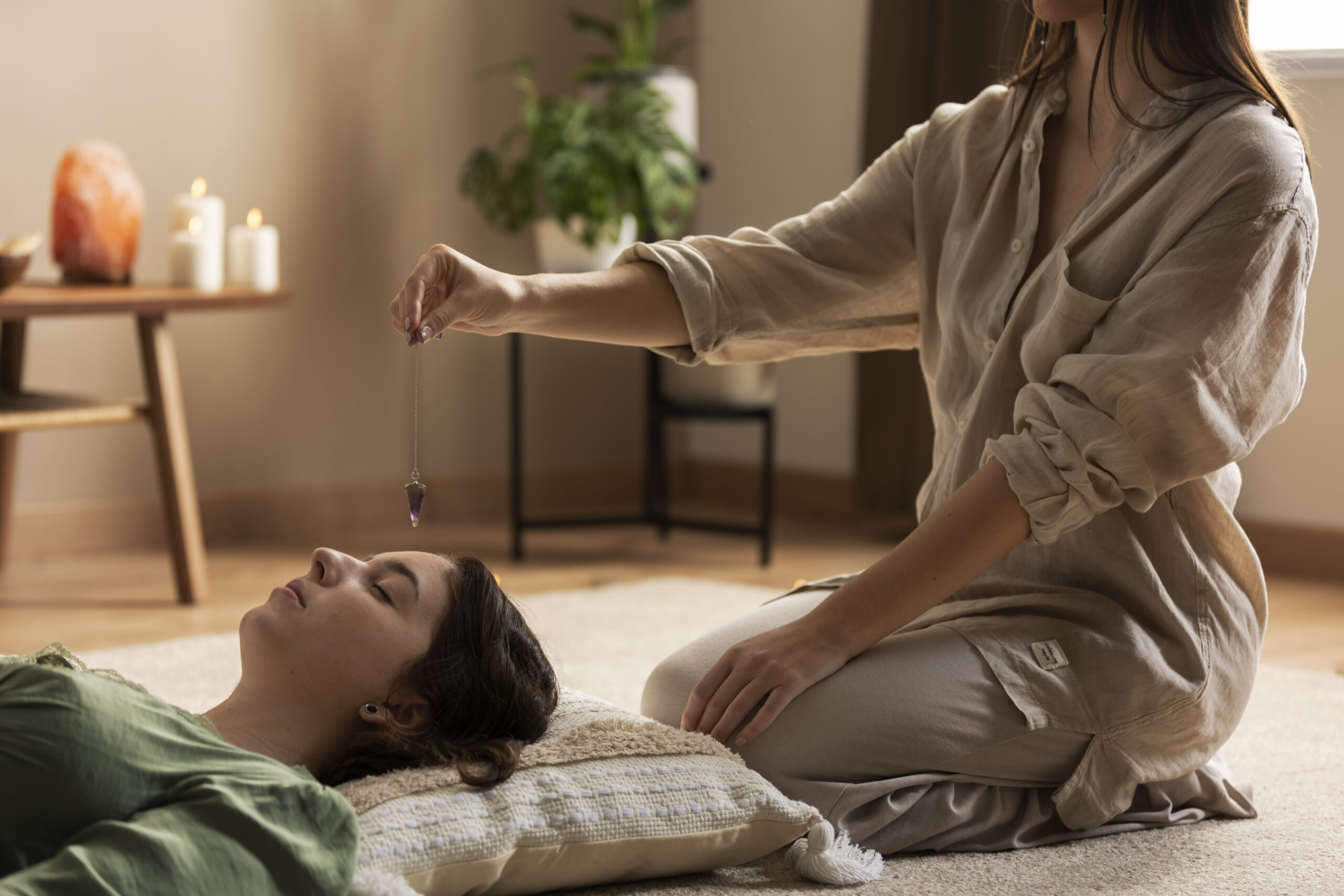 Une praticienne tient un pendule en cristal au-dessus d'une femme allongée les yeux fermés lors d'une séance de soin énergétique