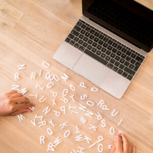 Agence Web 77 6 Mains manipulant des lettres en plastique blanc éparpillées sur un bureau en bois à côté d'un ordinateur portable