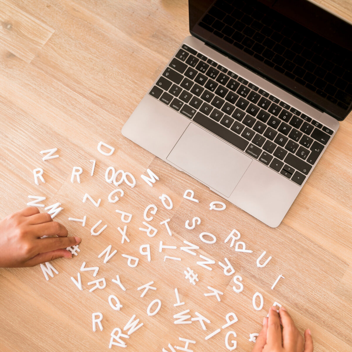 Mains manipulant des lettres en plastique blanc éparpillées sur un bureau en bois à côté d'un ordinateur portable