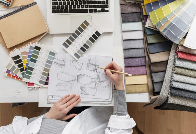 Designer d'intérieur dessinant des croquis de meubles, entouré d'échantillons de tissus et de nuanciers de couleurs sur un bureau