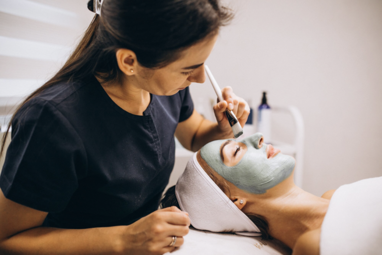 Esthéticienne appliquant un masque à l'argile vert sur le visage d'une cliente allongée en institut de beauté