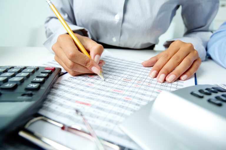 Une personne annotant un tableau de chiffres financiers avec un crayon, entourée de calculatrices sur un bureau