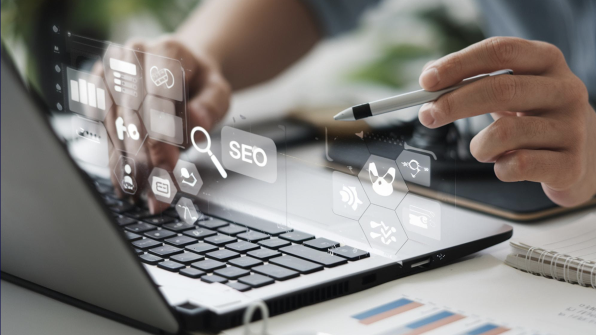 Personne utilisant un ordinateur portable avec des icônes numériques SEO et marketing flottant au-dessus du clavier