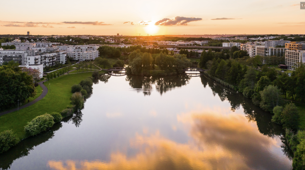 Vue aérienne d'un lac urbain au coucher du soleil, entouré de parcs verdoyants et d'immeubles résidentiels