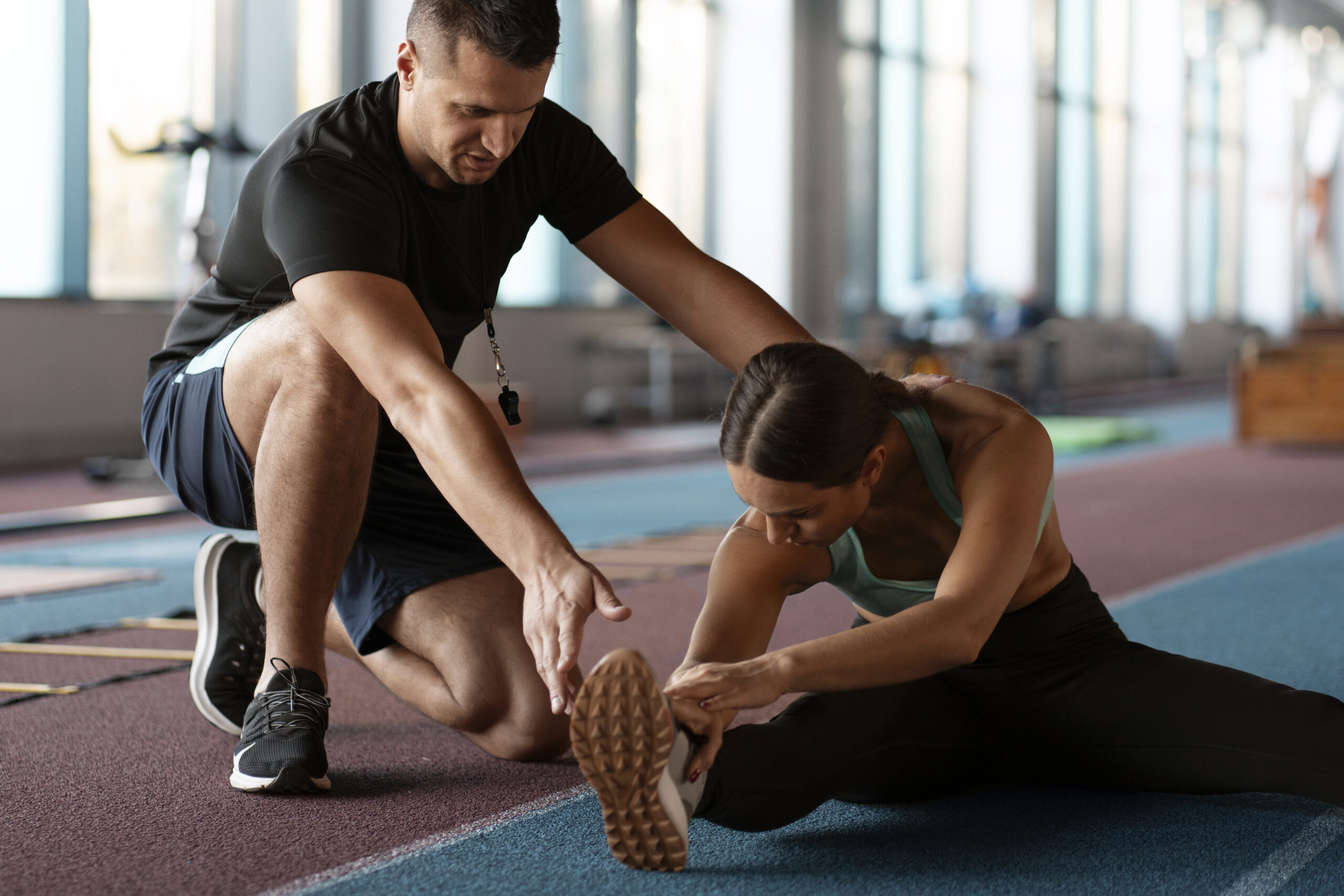 Un coach sportif aide une femme à effectuer un étirement des ischio-jambiers au sol dans une salle de sport