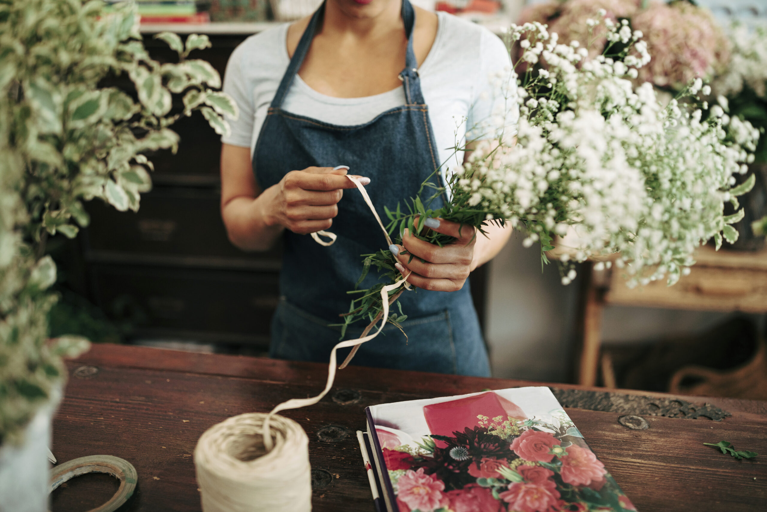 Fleuriste en tablier de jean attachant un bouquet de fleurs blanches avec un ruban dans un atelier floral