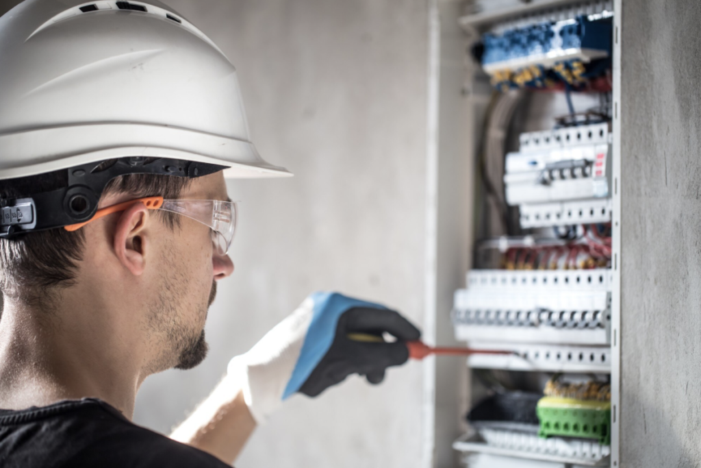 Électricien équipé d'un casque et de lunettes de protection travaillant sur un tableau électrique avec un tournevis