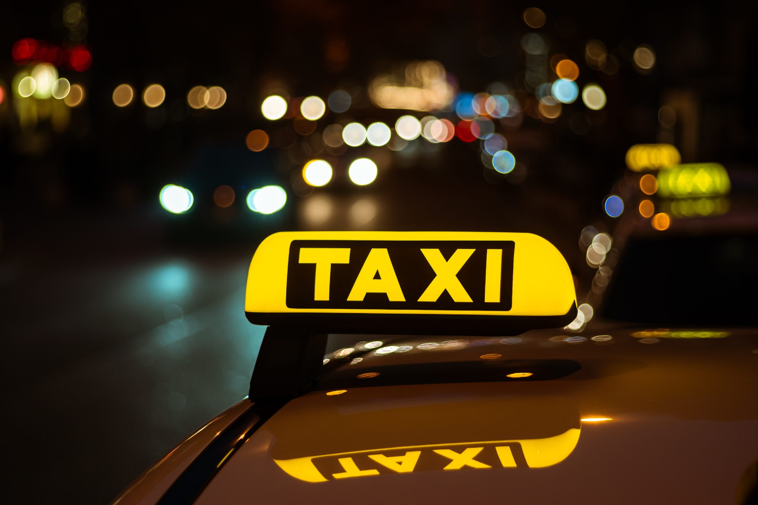 Enseigne lumineuse jaune « TAXI » sur le toit d'un véhicule, la nuit en ville avec des lumières floues en arrière-plan